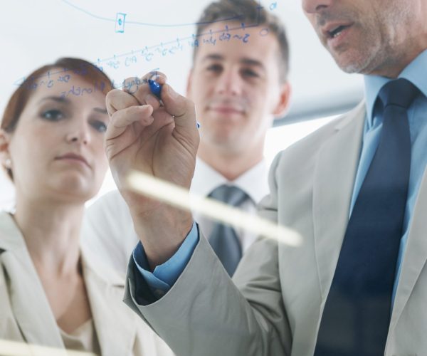 Glass wall, writing and business people with planning, ideas or brainstorming with financial growth. Leader, group or manager with employees or teaching with charts or graphs with startup or teamwork.